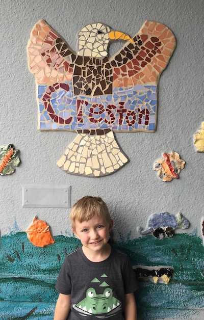 A kindergartener standing near an Eagle mosaic at Creston school.